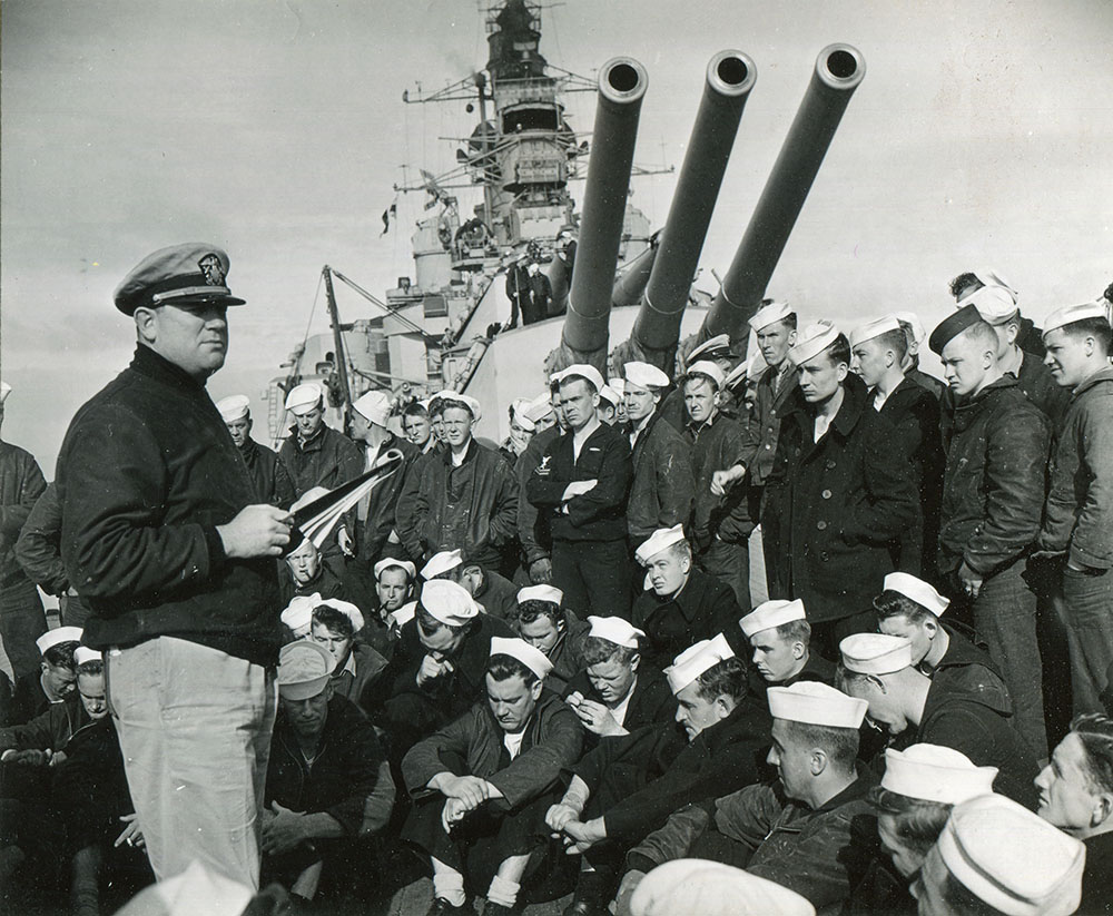 Aboard USS Nevada, a naval officer reads a letter from the Western Naval Task Force commander, Admiral Alan Kirk, describing when and where the naval bombardment will occur.