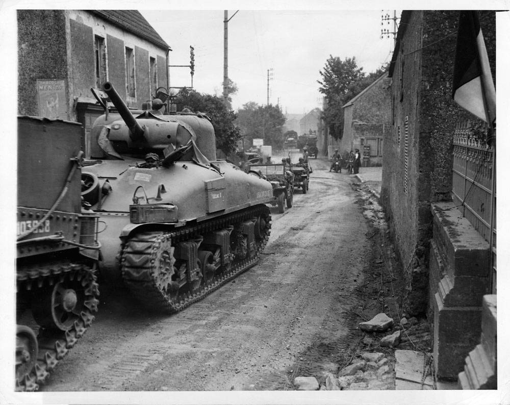 American tanks and jeeps roll through a liberated French town, on their way to engage the Germans.