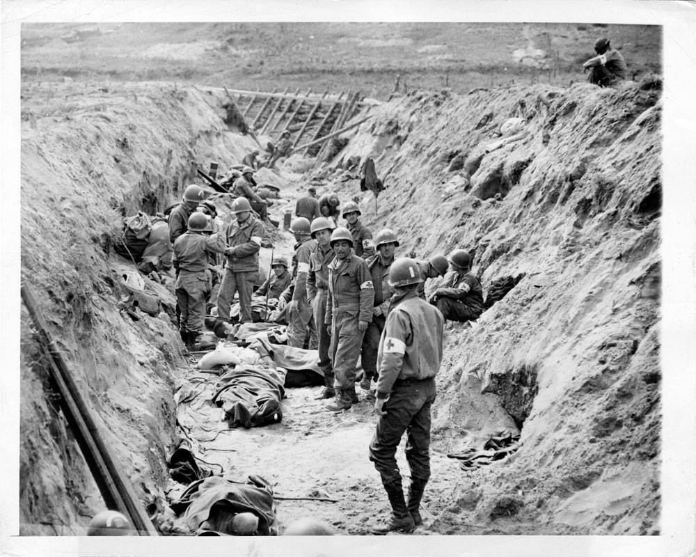 Somewhere in the beachhead area, American medical corpsmen convert a German anti-tank ditch into a temporary first aid station. Originally intended as invasion defenses, the ditches proved adequate for their improvised use.