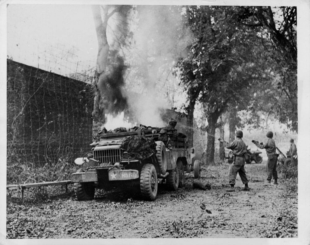 Yank soldiers at St. Lo work hard to put out the fire which destroyed this ammunition truck. Blaze extinguished, Yanks crossed the road under Nazi fire to continue the battle for the important communications center.