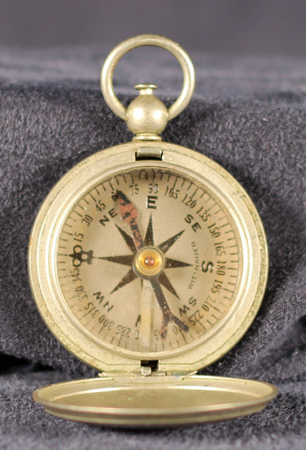 Metal compass is silver colored and circular. Inside the compass is a slightly rusted blue arrow. On top of the compass it says "U.S."