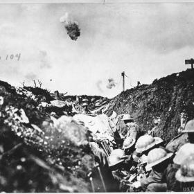 Photograph of a bomb exploding over soldiers in a trench. 