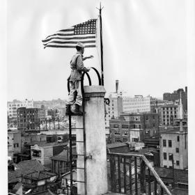 Signal Corps Officer, Lt. Bernard "Bud" Stapleton, raising an American flag over downtown Tokyo.
