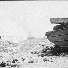 Marines taking shelter while an amphibious tractor burns in the distance on the island of Peleliu.