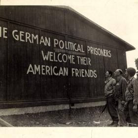 Survivor and American troops look at sign on building, welcoming American liberators.  