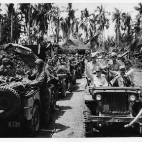 General MacArthur in a line of jeeps with soldiers.  