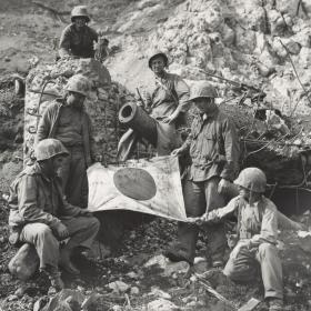 Marines hold Japanese flag on Iwo Jima.