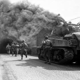 American soldiers run on a smoke filled street in Wernberg, Germany