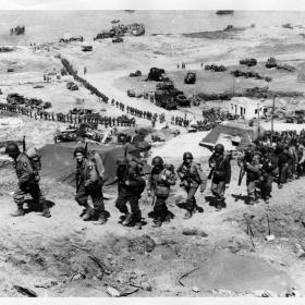 American troops climb the bluff overlooking Omaha Beach as units move inland to form the vanguard for the massive invasion of Nazi-dominated Europe.