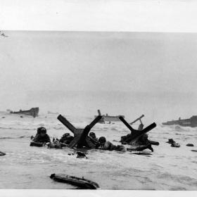 Steel and concrete obstacles, put up by the Germans to trap invasion craft, didn't stop Allied assault troops going ashore during the invasion of the French coast. To the contrary, these obstacles served as cover against enemy fire. Here, U.S. and British troops huddle against one of the "traps" as protection against enemy machine gun fire. 