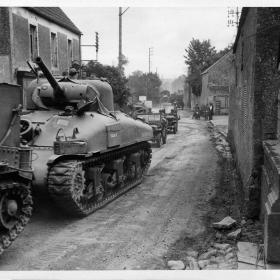 American tanks and jeeps roll through a liberated French town, on their way to engage the Germans.