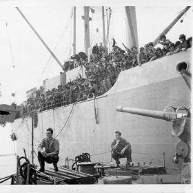 Allied assault troops wave jubilantly from aboard a transport which is pulling out from a British embarkation point enroute to France and the long-awaited invasion.