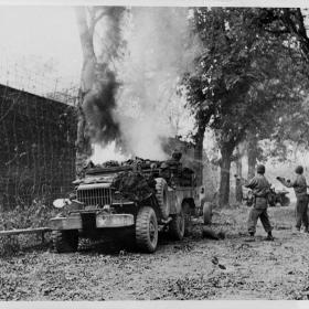Yank soldiers at St. Lo work hard to put out the fire which destroyed this ammunition truck. Blaze extinguished, Yanks crossed the road under Nazi fire to continue the battle for the important communications center.